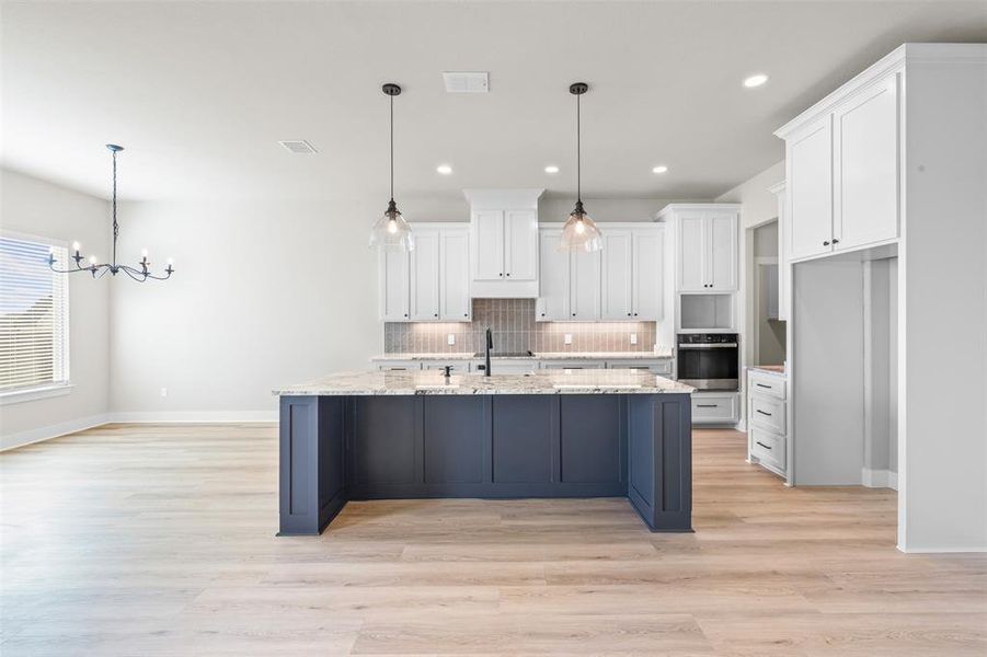 Kitchen with white cabinets, pendant lighting, light wood-type flooring, tasteful backsplash, and stainless steel oven