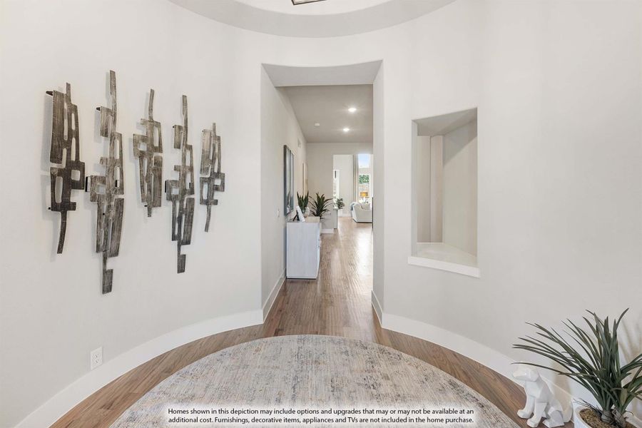 Curved foyer with hardwood floors, wall art, built-in niche, and hallway leading to living area