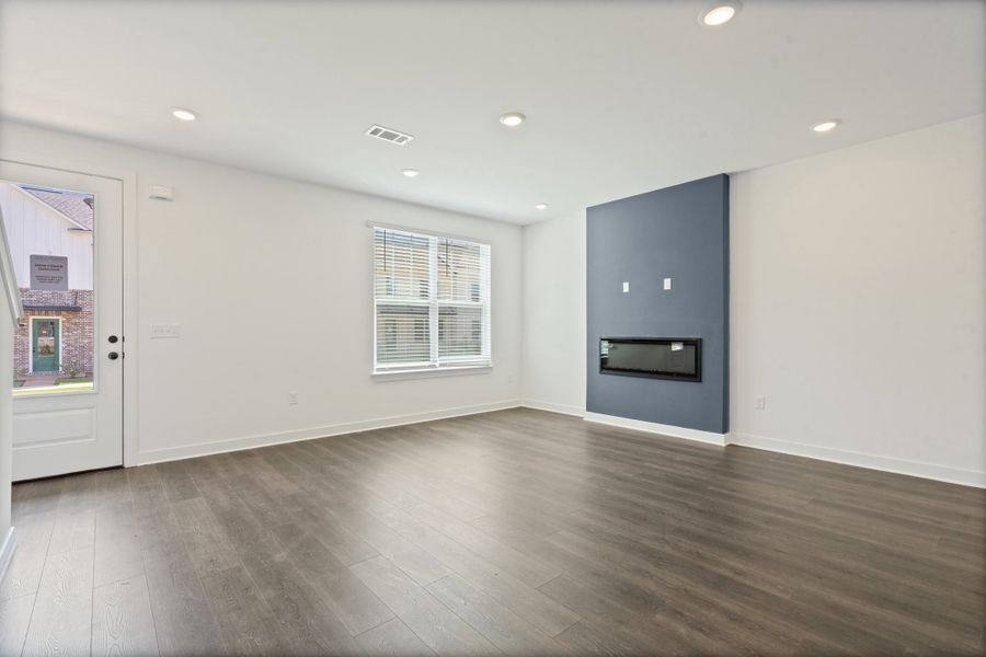 Recessed lighting, wood-finish flooring, a contemporary accent wall, an integrated fireplace, and a glass-paneled door