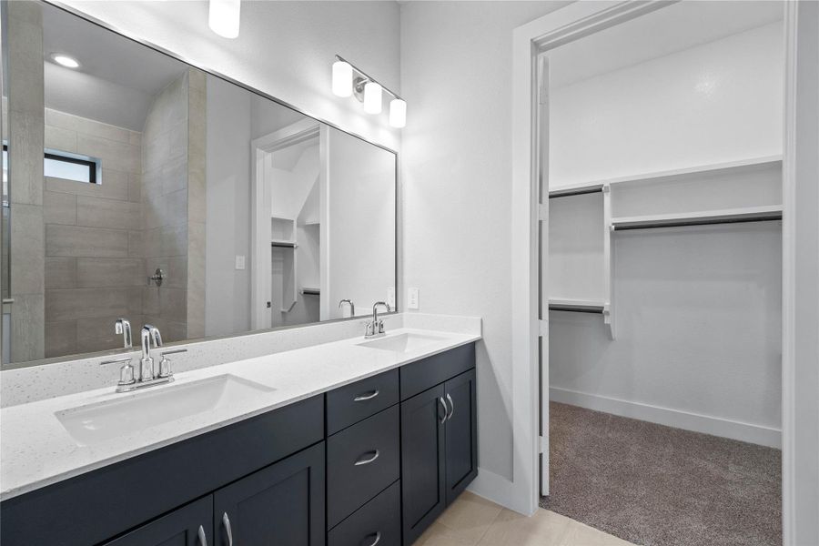 This stunningly updated primary bathroom is truly move-in ready! It features stained cabinetry with light countertops, dual vanities, a large mirror, high ceilings, custom paint, tile flooring, and sleek modern finishes throughout.