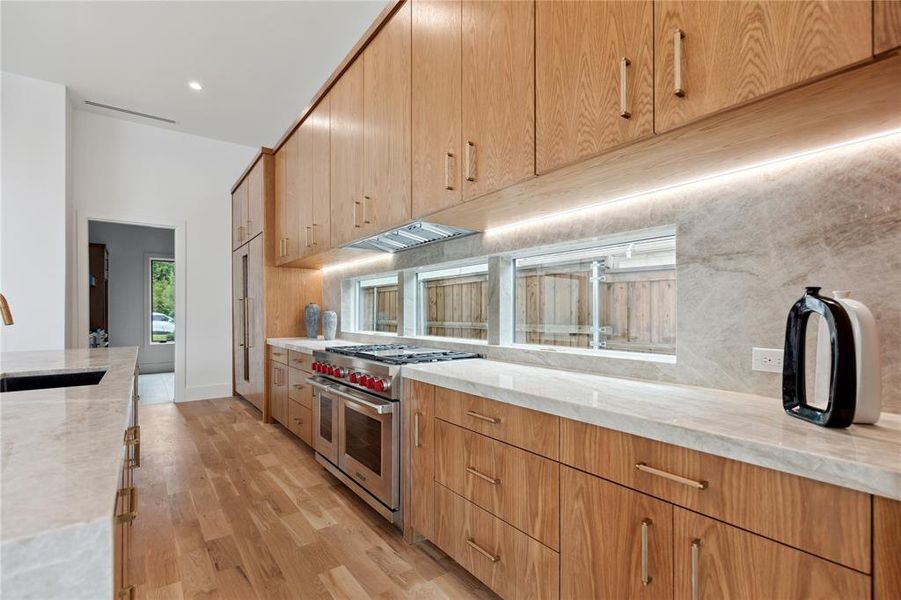 Kitchen with light stone counters, sink, light hardwood / wood-style floors, backsplash, and range with two ovens