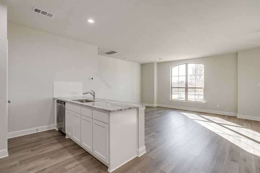 Kitchen with a peninsula, light stone counters, white cabinetry, light wood-style flooring, and open floor plan