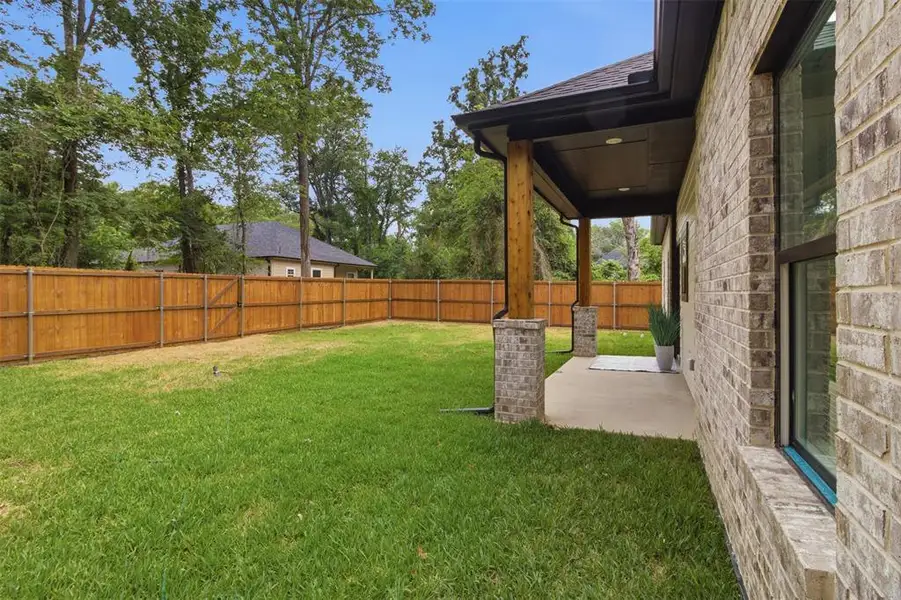 Expansive green lawn with a newly installed wood privacy fence, featuring a covered patio with brick columns, wood posts, and recessed lighting