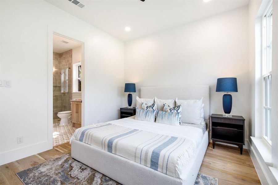 Bright sleeping area featuring light wood-finish flooring, recessed lighting, and a window with white sills Bright sleeping area featuring light wood-finish flooring, recessed lighting, and a window with white sills