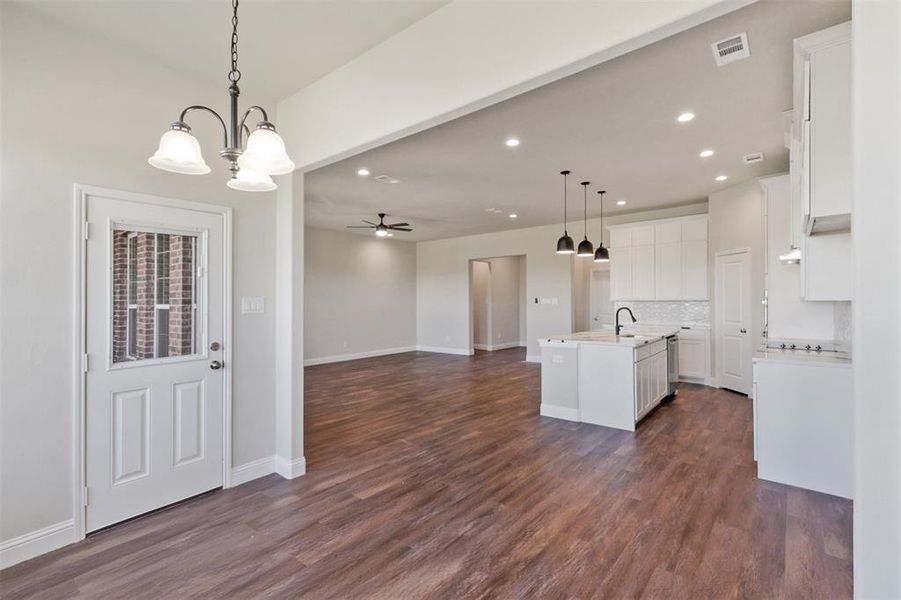 Kitchen with white cabinetry, dark wood-type flooring, decorative light fixtures, a kitchen island with sink, and ceiling fan with notable chandelier