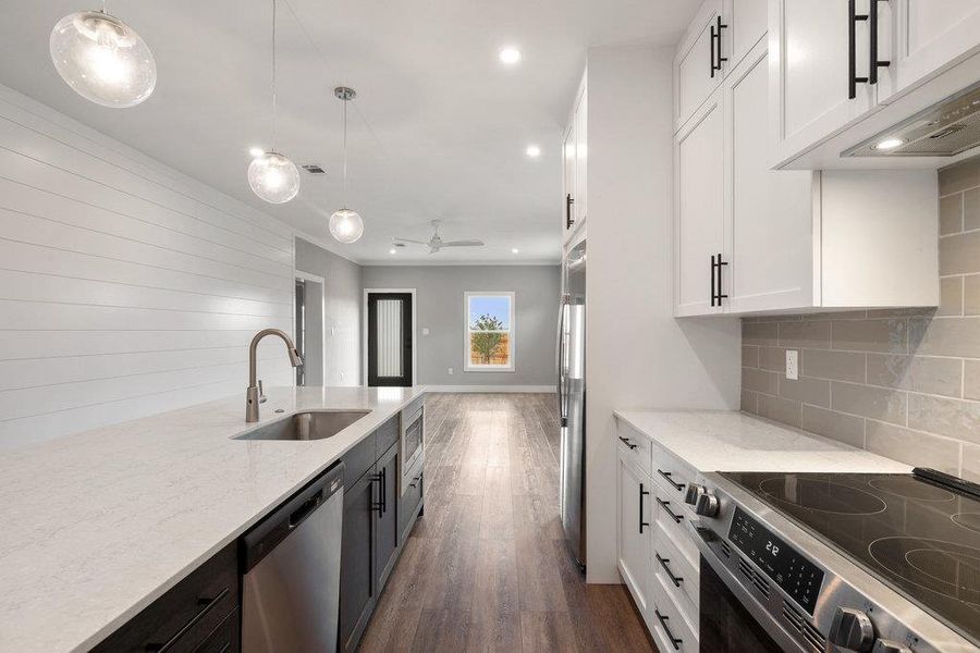 Kitchen featuring stainless steel appliances, light stone counters, dark wood-type flooring, a ceiling fan, and hanging light fixtures