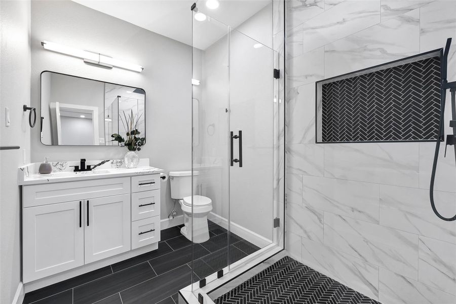 Modern bathroom featuring a sleek glass-enclosed shower with herringbone tile accents, a white vanity with black fixtures, and stylish lighting.