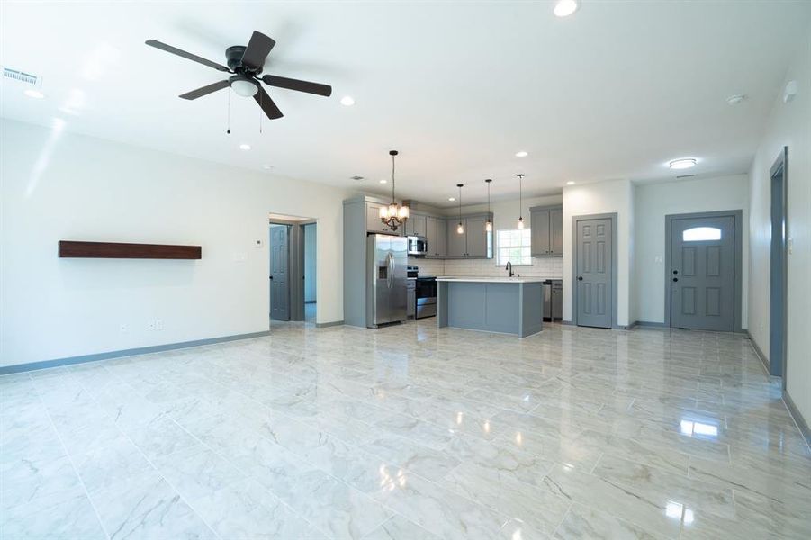 Kitchen with appliances with stainless steel finishes, ceiling fan with notable chandelier, light tile patterned floors, a center island, and gray cabinets