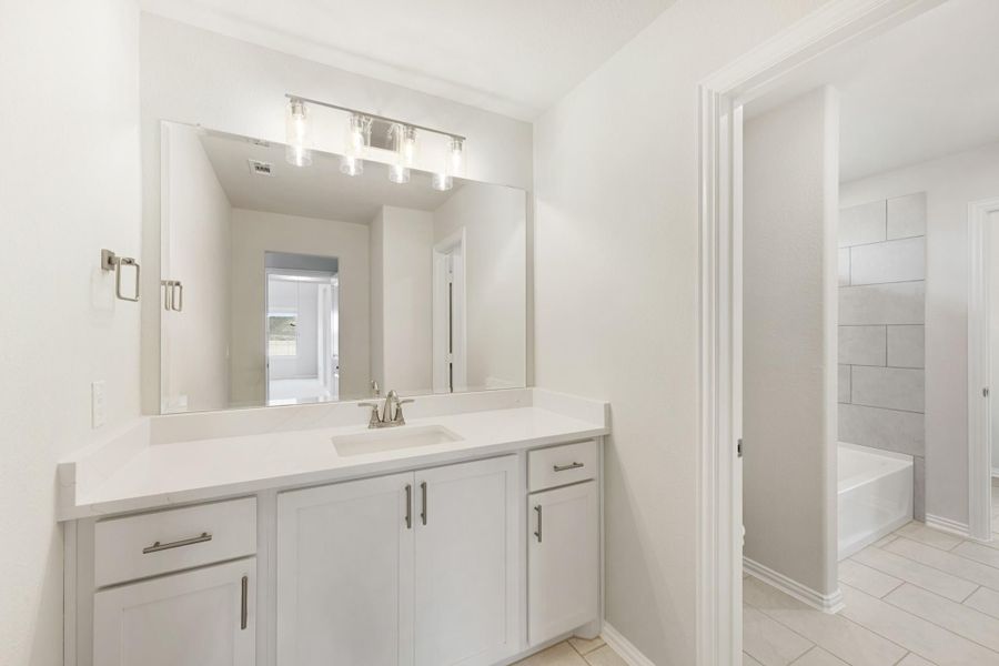 Bathroom with white vanity, single sink, large mirror, and soaking tub visible through doorway