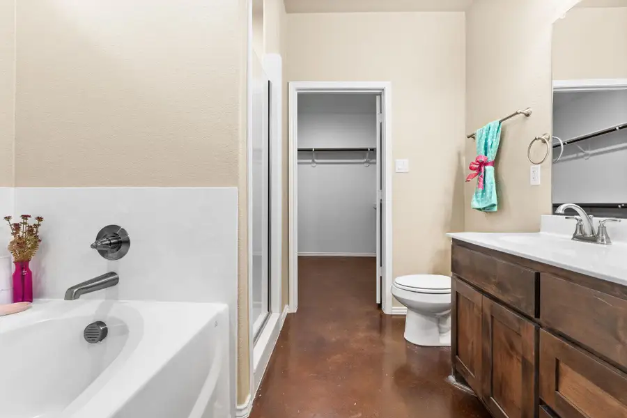 Full bathroom featuring finished concrete floors, a spacious closet, vanity, a bath, and a stall shower