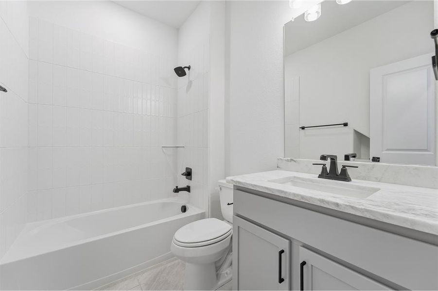 Bathroom featuring a white bathtub, vertical subway tile shower surround, matte black fixtures, a single-sink vanity with light gray cabinetry, and a stone-finish countertop