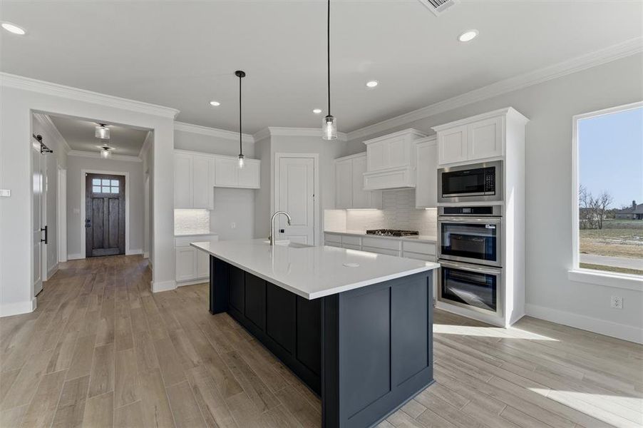 Kitchen featuring backsplash, light wood-type flooring, an island with sink, stainless steel appliances, and two tone color scheme