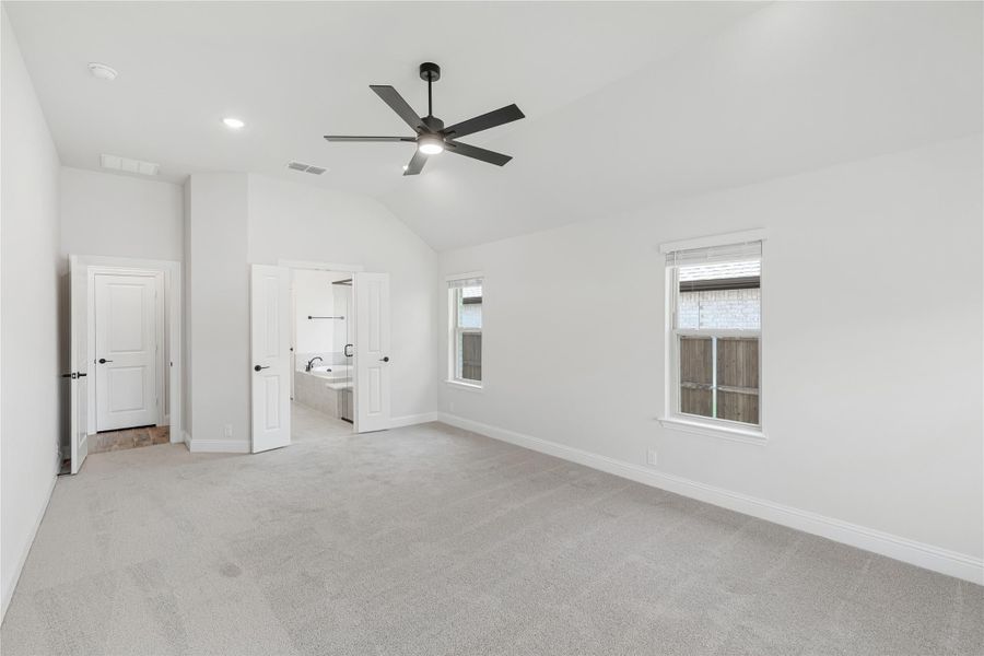 Spacious bedroom with vaulted ceiling, ceiling fan, carpet flooring, and ensuite bathroom access