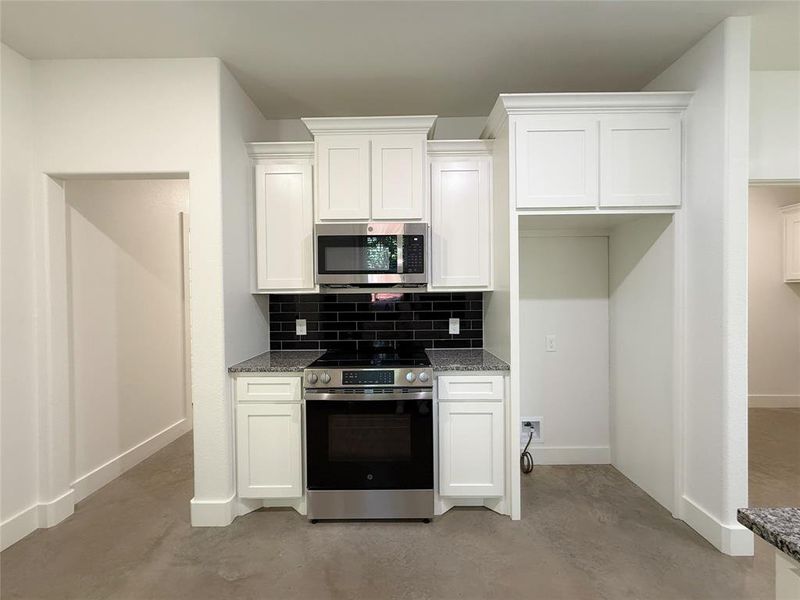 Kitchen featuring stainless steel appliances, concrete flooring, white cabinetry, and backsplash