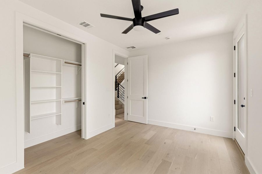 Bright room featuring light wood-finish flooring, a contemporary black ceiling fan, and a built-in closet organization system