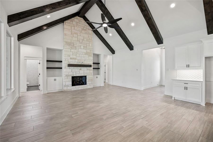Unfurnished living room with ceiling fan, a stone fireplace, beamed ceiling, high vaulted ceiling, and light wood-style floors Unfurnished living room with ceiling fan, a stone fireplace, beamed ceiling, high vaulted ceiling, and light wood-style floors