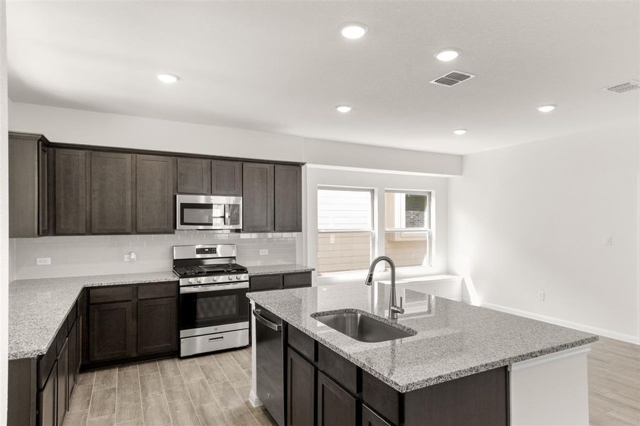 Kitchen with stainless steel appliances, backsplash, a center island with sink, a sink, and visible vents