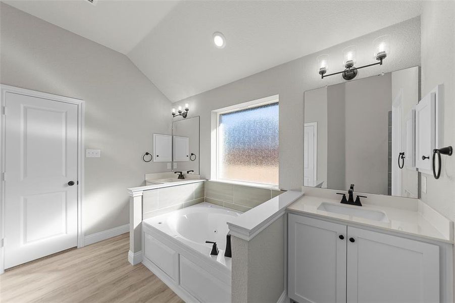 Full bath with two vanities, a bath, lofted ceiling, light wood-type flooring, and recessed lighting