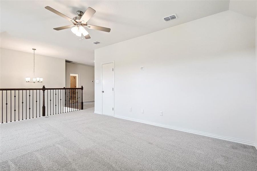 Carpeted empty room featuring ceiling fan with notable chandelier and vaulted ceiling