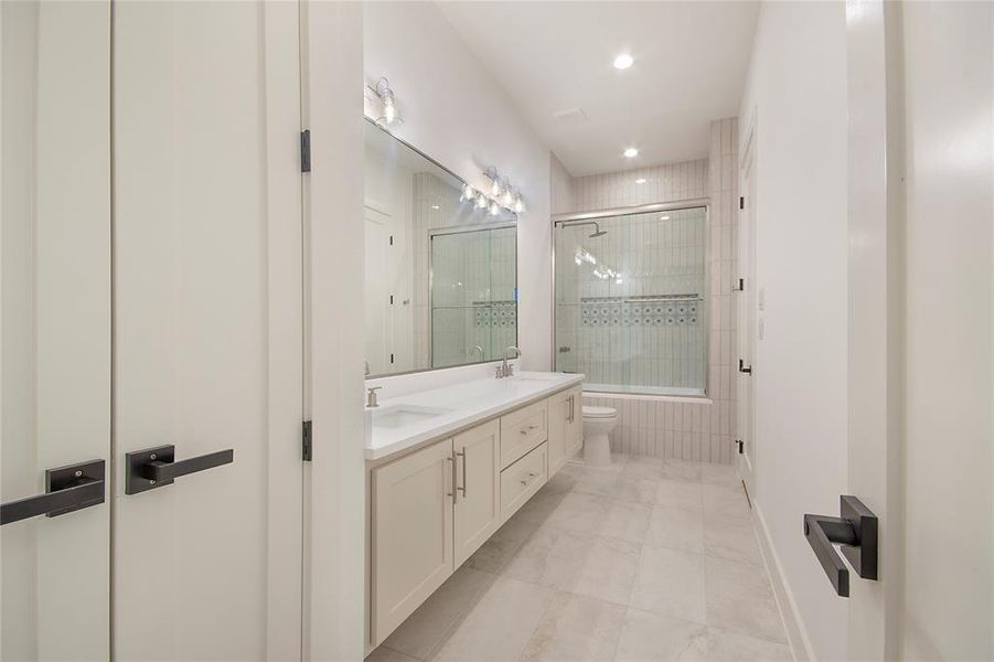 Full bath featuring double vanity, light tile patterned flooring, recessed lighting, and tiled shower / bath combo