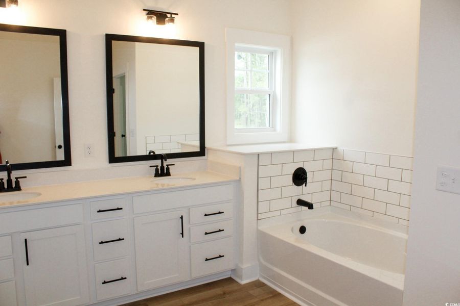 Full bath featuring double vanity, a garden tub, and light wood-style floors