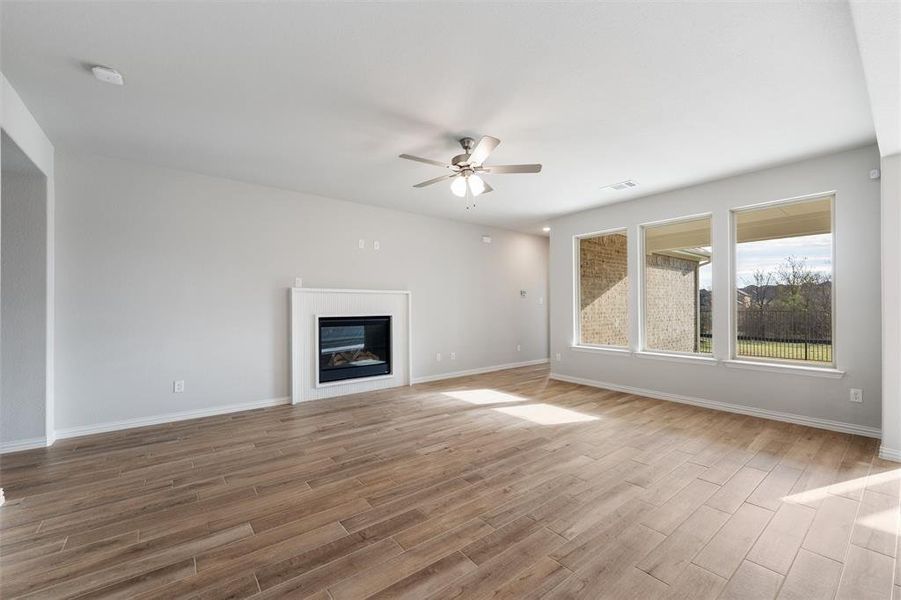 Unfurnished living room featuring light wood-type flooring, ceiling fan, and a glass covered fireplace