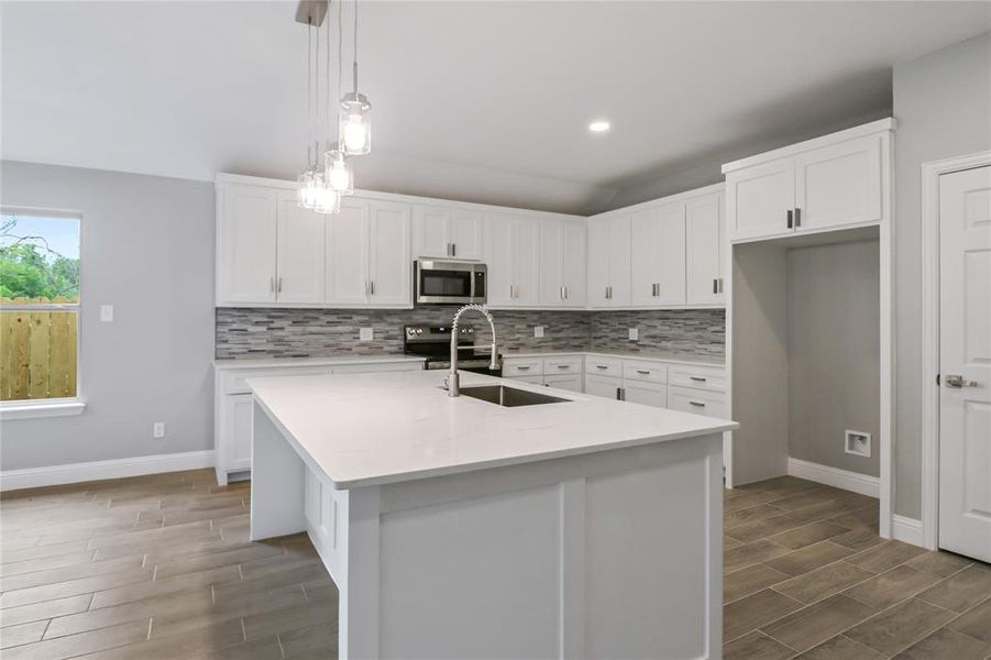 Kitchen featuring appliances with stainless steel finishes, an island with sink, decorative backsplash, and sink