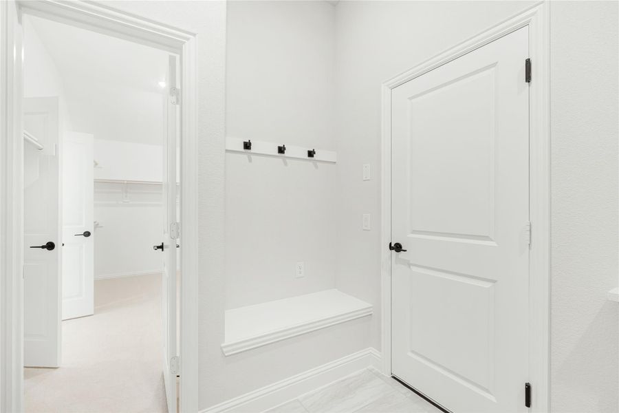 Mudroom with built-in bench, wall hooks, and white doors leading to carpeted hallway