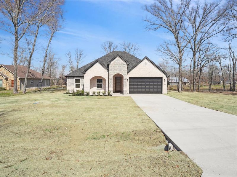 French country style house with stone siding, an attached garage, driveway, a front yard, and brick siding