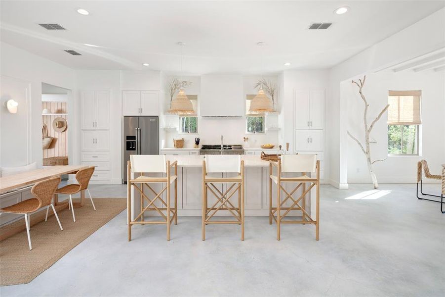 Kitchen with a kitchen bar, a kitchen island, high quality fridge, white cabinets, and ventilation hood Kitchen with a kitchen bar, a kitchen island, high quality fridge, white cabinets, and ventilation hood