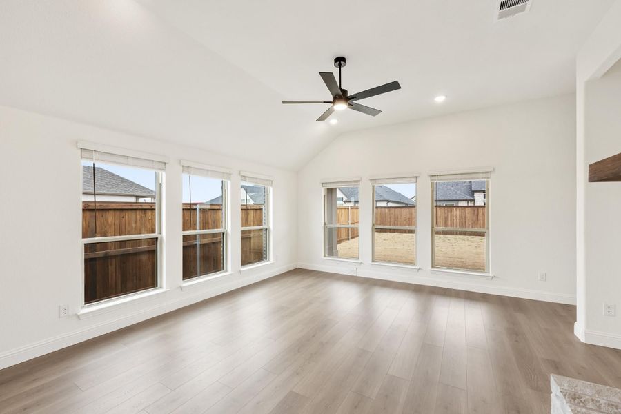 Empty living room with vaulted ceiling, ceiling fan, hardwood floors, and large windows overlooking backyard fence Empty living room with vaulted ceiling, ceiling fan, hardwood floors, and large windows overlooking backyard fence