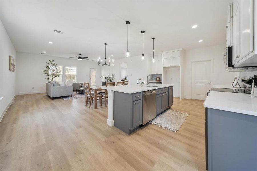 Kitchen with hanging light fixtures, light wood-type flooring, stainless steel appliances, a kitchen island with sink, and white cabinets