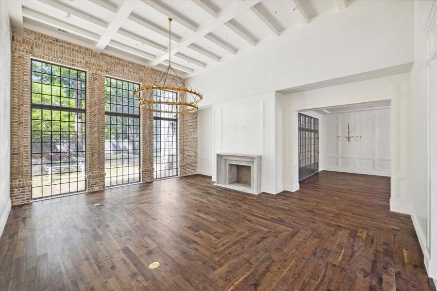 The great room features elegant wood flooring, a fireplace with a stone mantel, tall iron windows nestled in the exposed brick walls, and a stunning gold two-tiered chandelier.