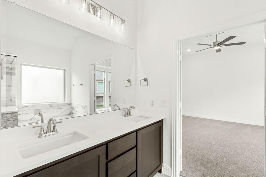 Bathroom with double sink vanity, dark wood cabinets, white countertop, marble backsplash, and large mirror with overhead lighting. Bathroom with double sink vanity, dark wood cabinets, white countertop, marble backsplash, and large mirror with overhead lighting.