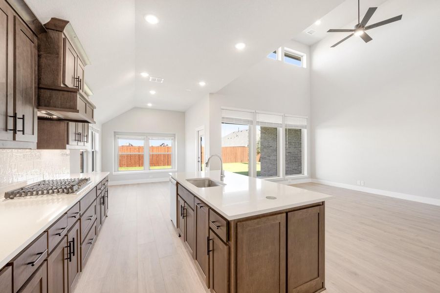 Open kitchen with dark wood cabinets, center island with sink, vaulted ceiling, and light hardwood floors Open kitchen with dark wood cabinets, center island with sink, vaulted ceiling, and light hardwood floors