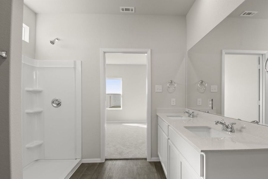 Image of a primary bathroom with cream walls, white cabinets, a white jack and jill vanity, a large mirror and a walk-in shower