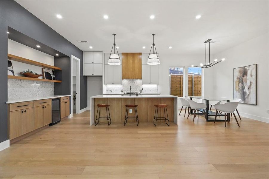Kitchen with open shelves, two tone color scheme, a kitchen bar, light wood-style floors, and decorative backsplash