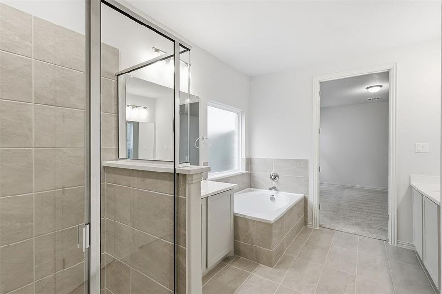 Full bath featuring two vanities, a stall shower, a bath, light tile patterned flooring, and light carpet