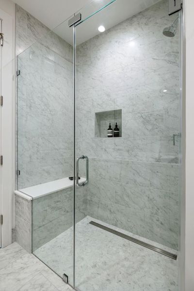 Frameless glass shower features a full marble tile surround and built-in bench seating.