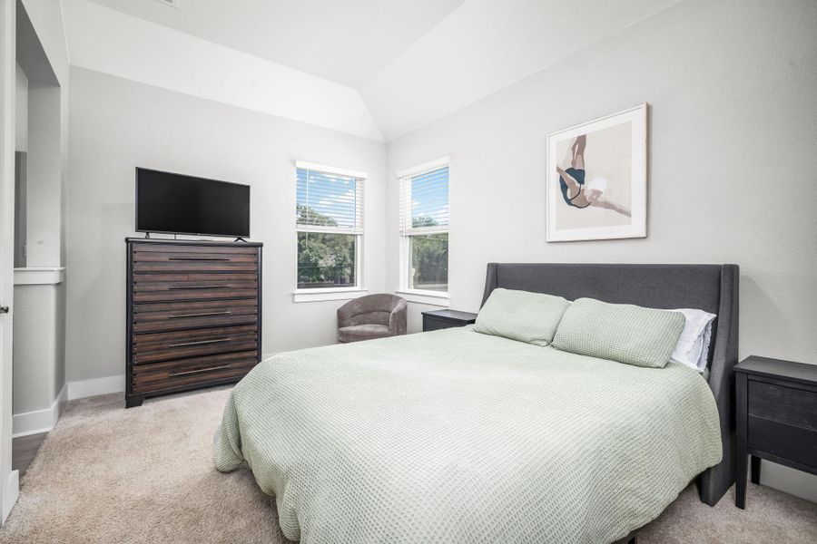 An inviting bedroom features a cozy bed, ample natural light, and a chair, perfect for relaxation.