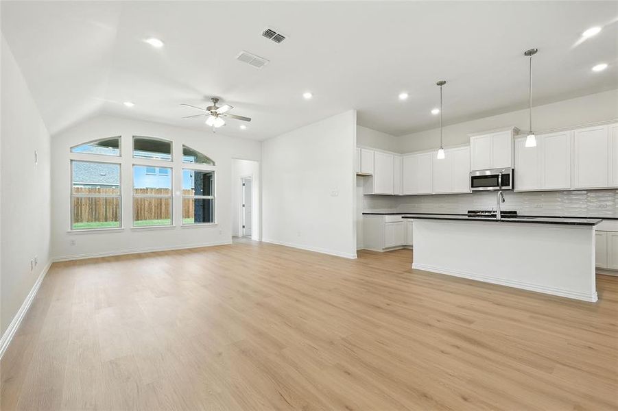 Kitchen with open floor plan, white cabinets, dark countertops, a kitchen island with sink, and stainless steel microwave