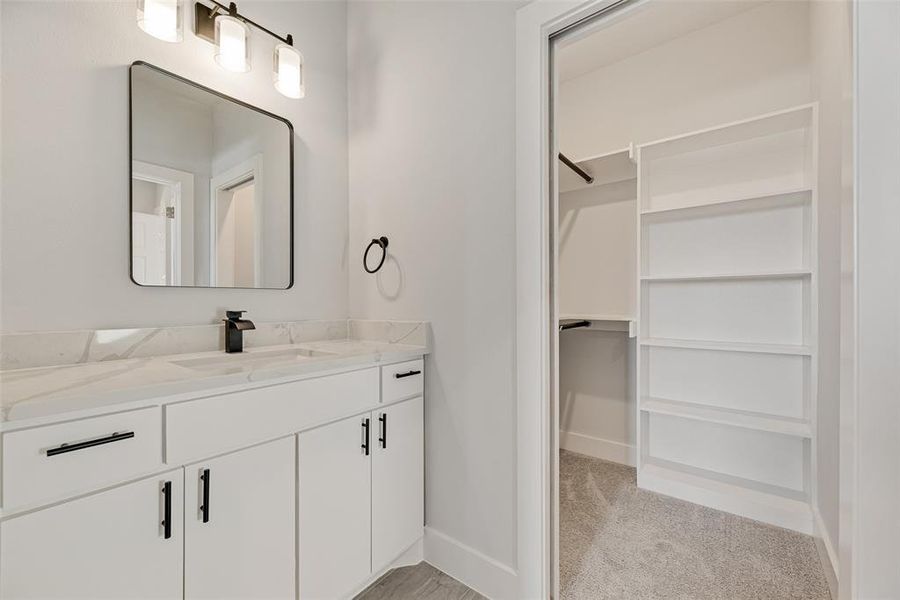 Bathroom featuring vanity, a walk in closet, and light colored carpet Bathroom featuring vanity, a walk in closet, and light colored carpet