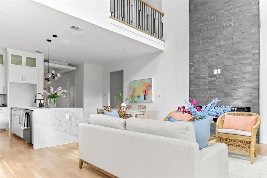 Living room with light wood-type flooring, a towering ceiling, a fireplace, and an inviting chandelier