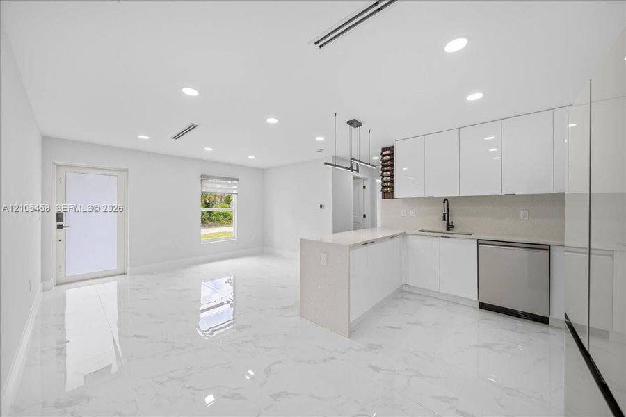 Open-concept layout featuring white high-gloss cabinetry, stainless steel dishwasher, integrated wine storage, white quartz countertops, and recessed lighting Open-concept layout featuring white high-gloss cabinetry, stainless steel dishwasher, integrated wine storage, white quartz countertops, and recessed lighting