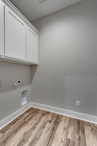 Clothes washing area with wood-type flooring, cabinets, and electric dryer hookup