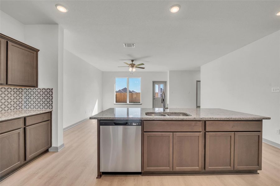 Kitchen featuring stainless steel dishwasher, light stone counters, backsplash, light wood finished floors, and recessed lighting
