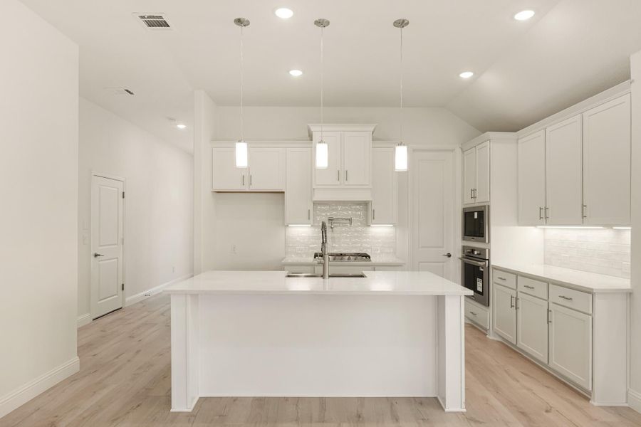White kitchen with large center island, pendant lights, tile backsplash, and light wood floors