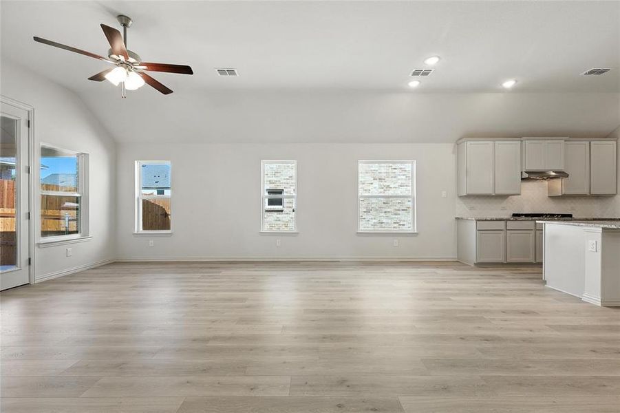 Unfurnished living room featuring lofted ceiling, ceiling fan, healthy amount of natural light, light wood finished floors, and recessed lighting Unfurnished living room featuring lofted ceiling, ceiling fan, healthy amount of natural light, light wood finished floors, and recessed lighting