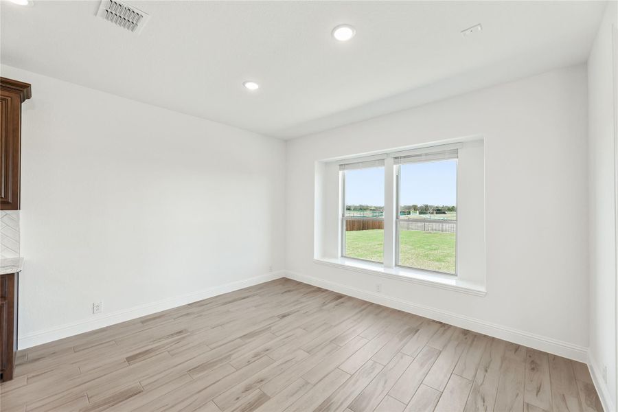 Empty dining or breakfast room with light wood floors, white walls, and large window overlooking a backyard Empty dining or breakfast room with light wood floors, white walls, and large window overlooking a backyard