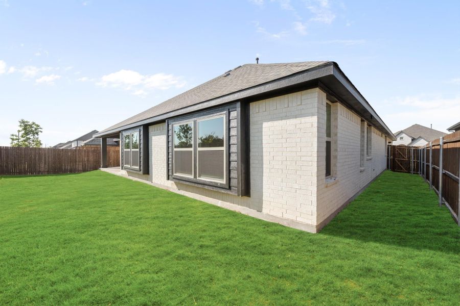 Rear exterior of single-story brick home with large windows, green lawn, and wood privacy fence. Rear exterior of single-story brick home with large windows, green lawn, and wood privacy fence.